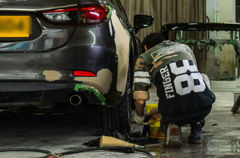 Chapista preparando la aleta trasera de un coche con masilla y cinta