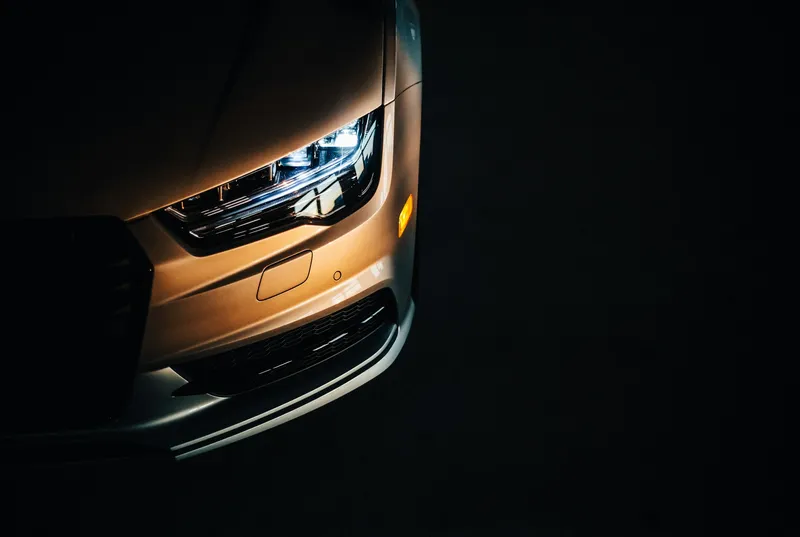 Faro delantero de un coche cobrizo iluminado en la oscuridad