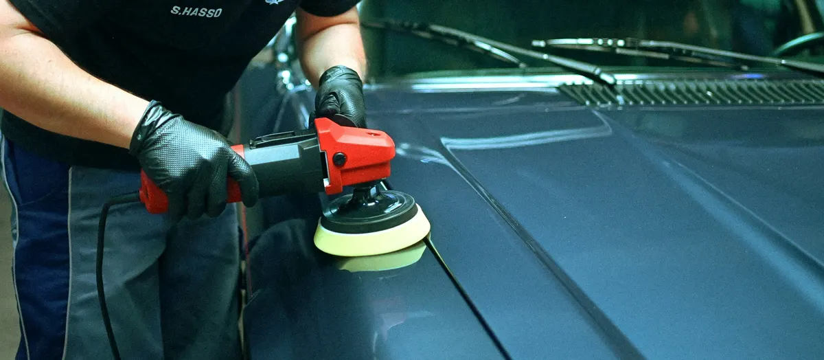 Pulido del capó de un coche oscuro con una pulidora roja