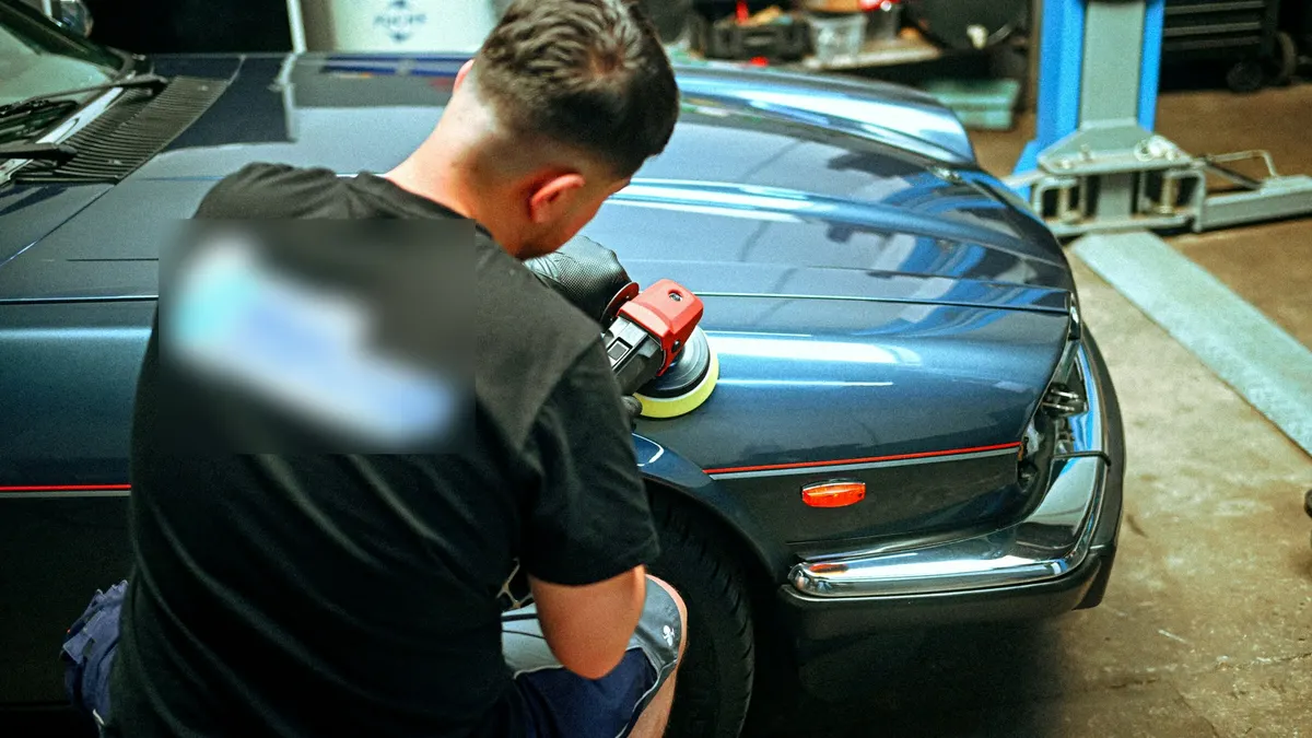 Operario puliendo el capó de un coche azul clásico en el taller